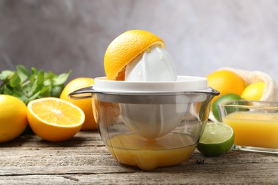 Photo of Plastic juicer and fresh oranges on wooden table, closeup