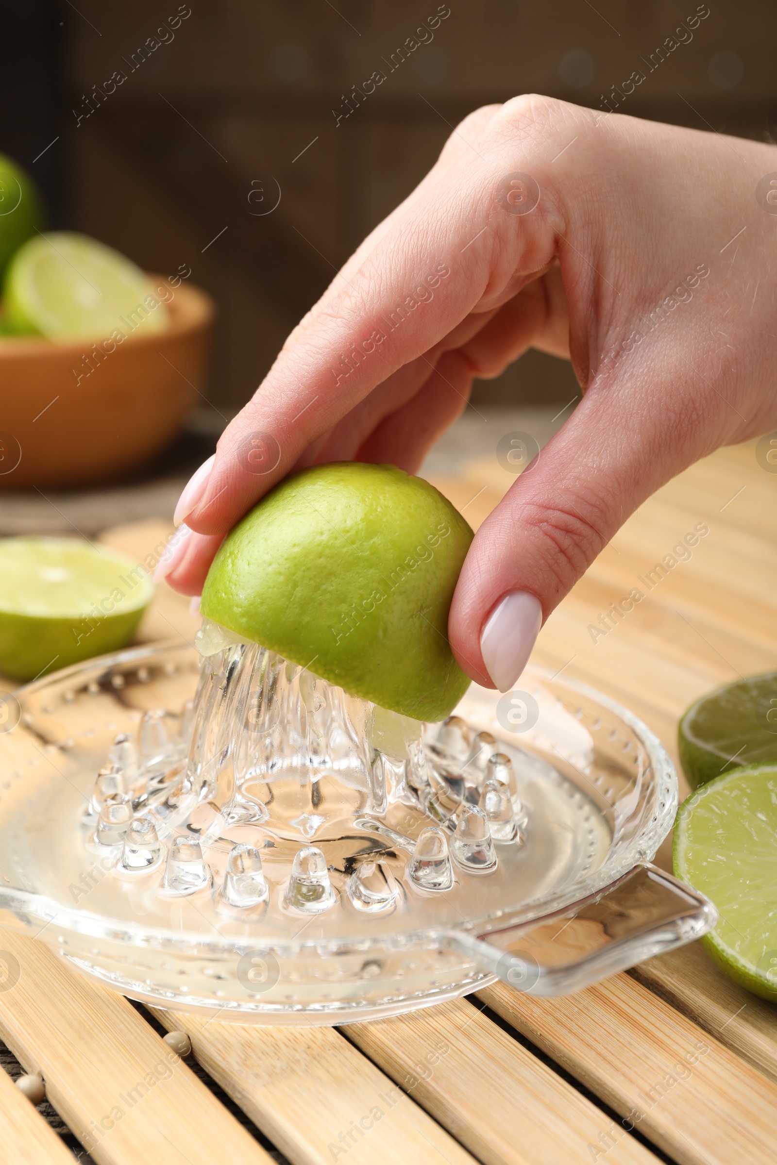 Photo of Woman squeezing juice of fresh lime with juicer at wooden table, closeup