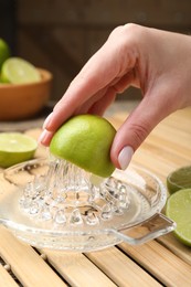 Photo of Woman squeezing juice of fresh lime with juicer at wooden table, closeup