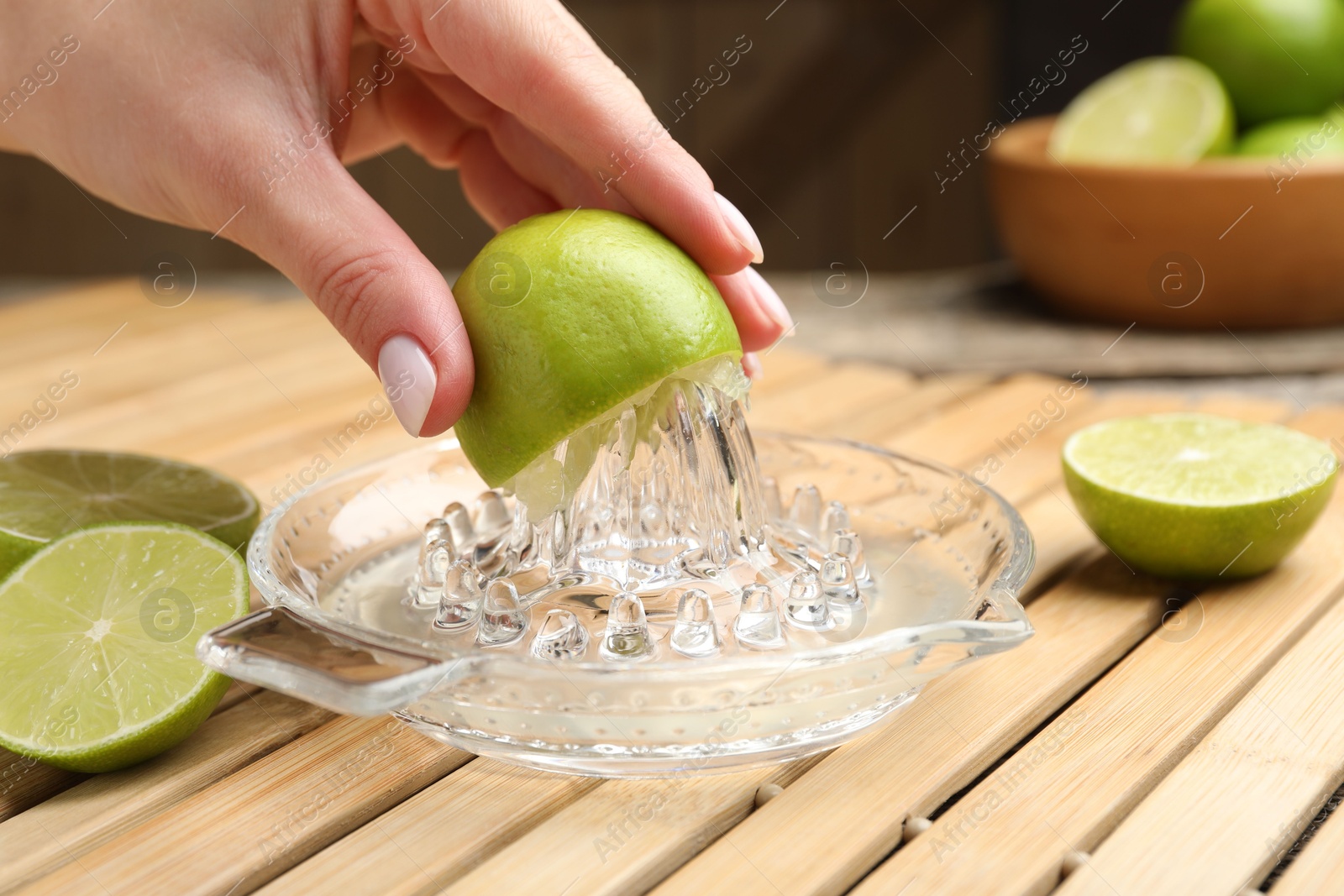 Photo of Woman squeezing juice of fresh lime with juicer at wooden table, closeup