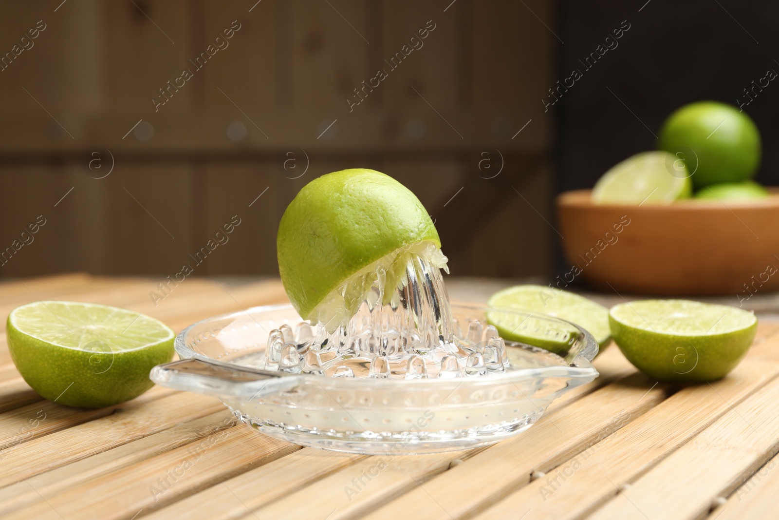 Photo of Glass juicer and fresh limes on wooden table, closeup