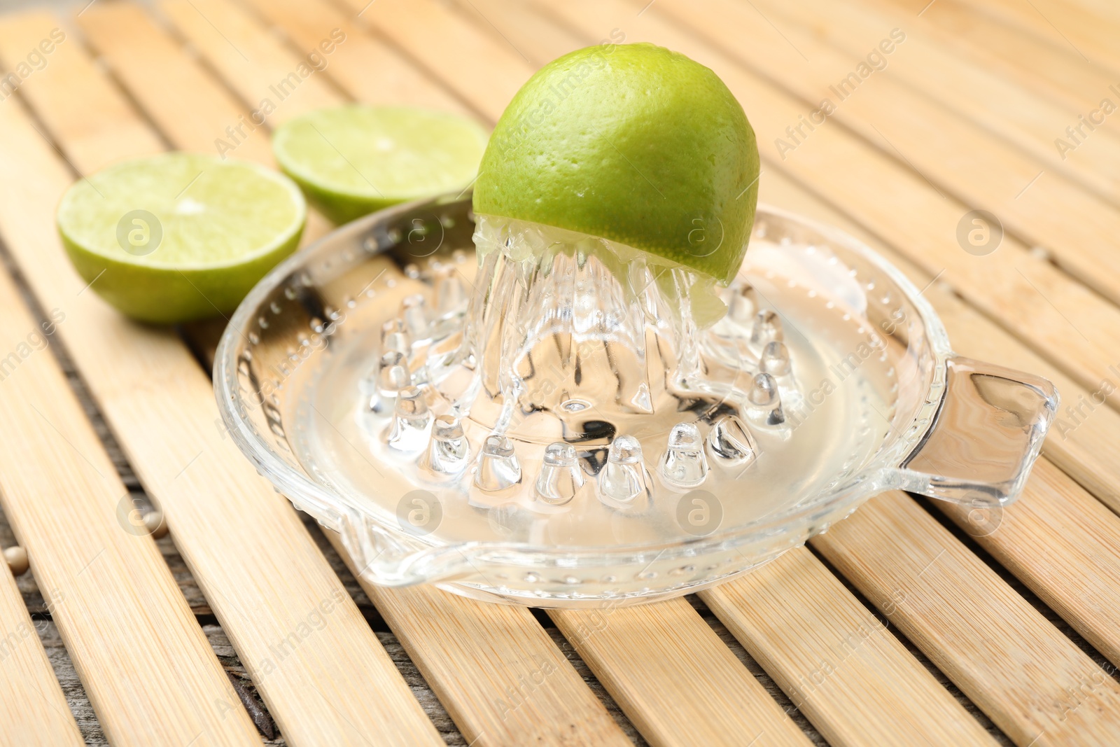 Photo of Glass juicer and fresh limes on wooden table, closeup