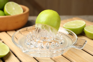 Photo of Glass juicer and fresh limes on wooden table, closeup