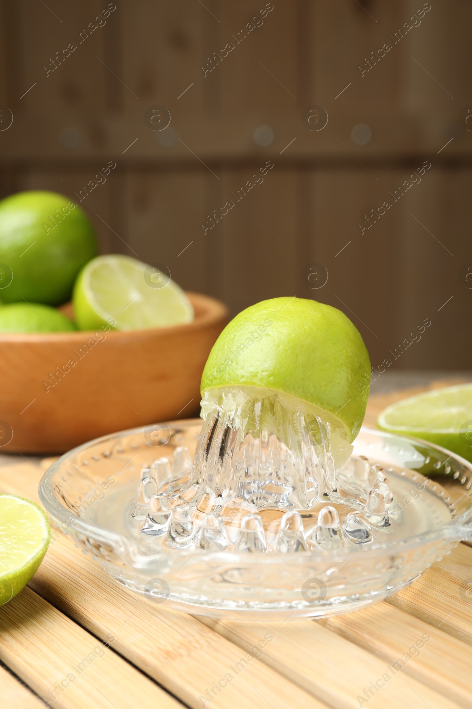 Photo of Glass juicer and fresh limes on wooden table, closeup