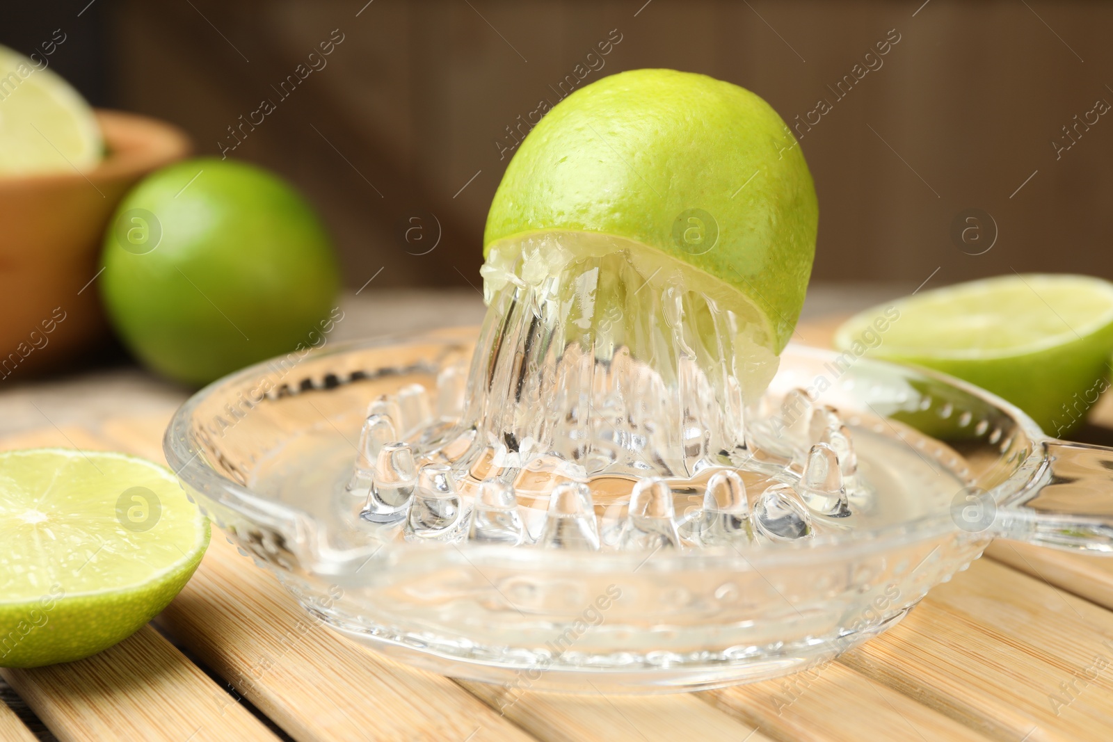 Photo of Glass juicer and fresh limes on wooden table, closeup