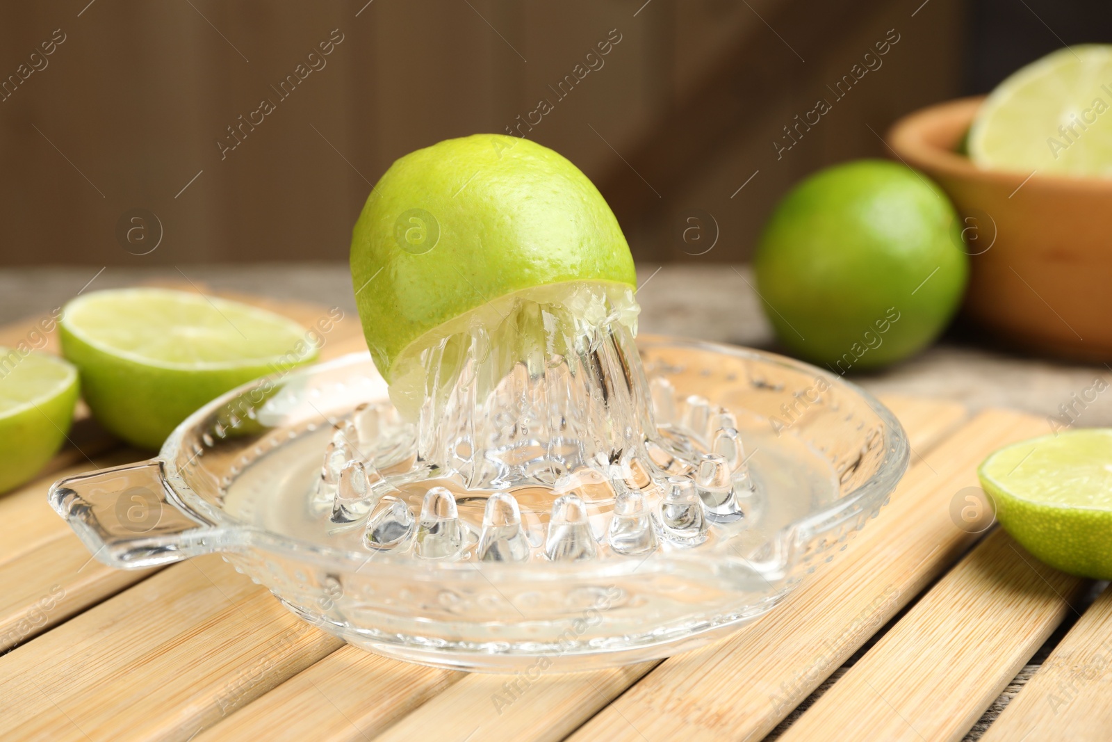 Photo of Glass juicer and fresh limes on wooden table, closeup