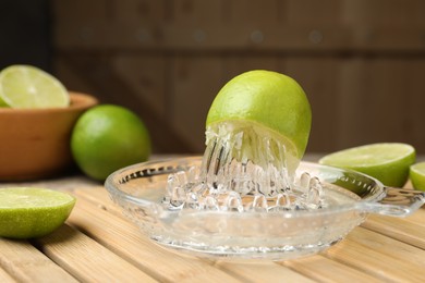 Photo of Glass juicer and fresh limes on wooden table, closeup