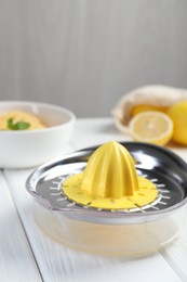 Photo of Plastic juicer and fresh lemons on white wooden table, closeup