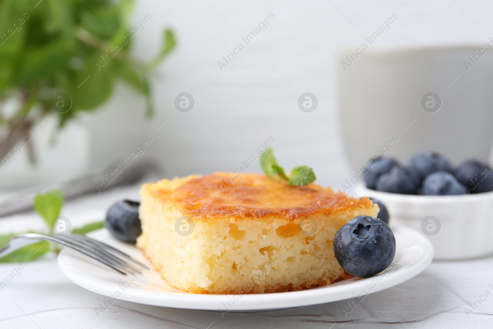 Photo of Slice of tasty semolina cake served on white textured table, closeup