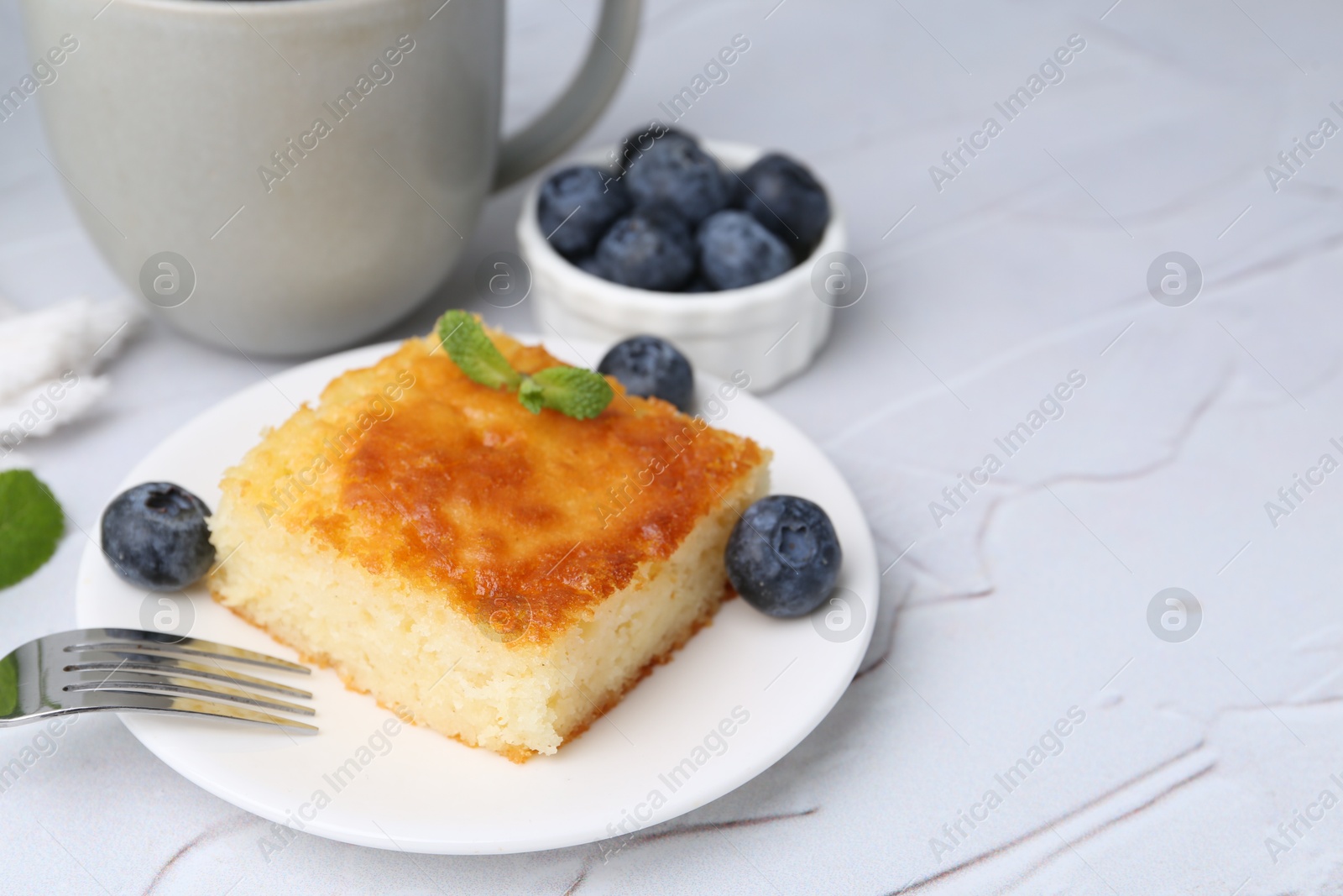 Photo of Slice of tasty semolina cake served on white textured table, closeup. Space for text