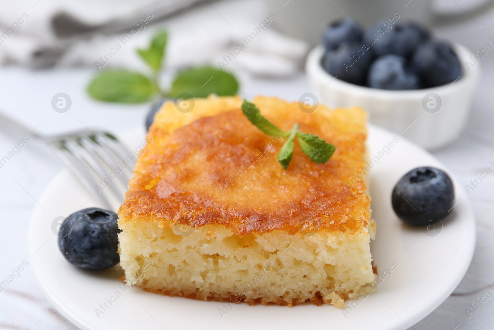 Photo of Slice of tasty semolina cake served on white textured table, closeup