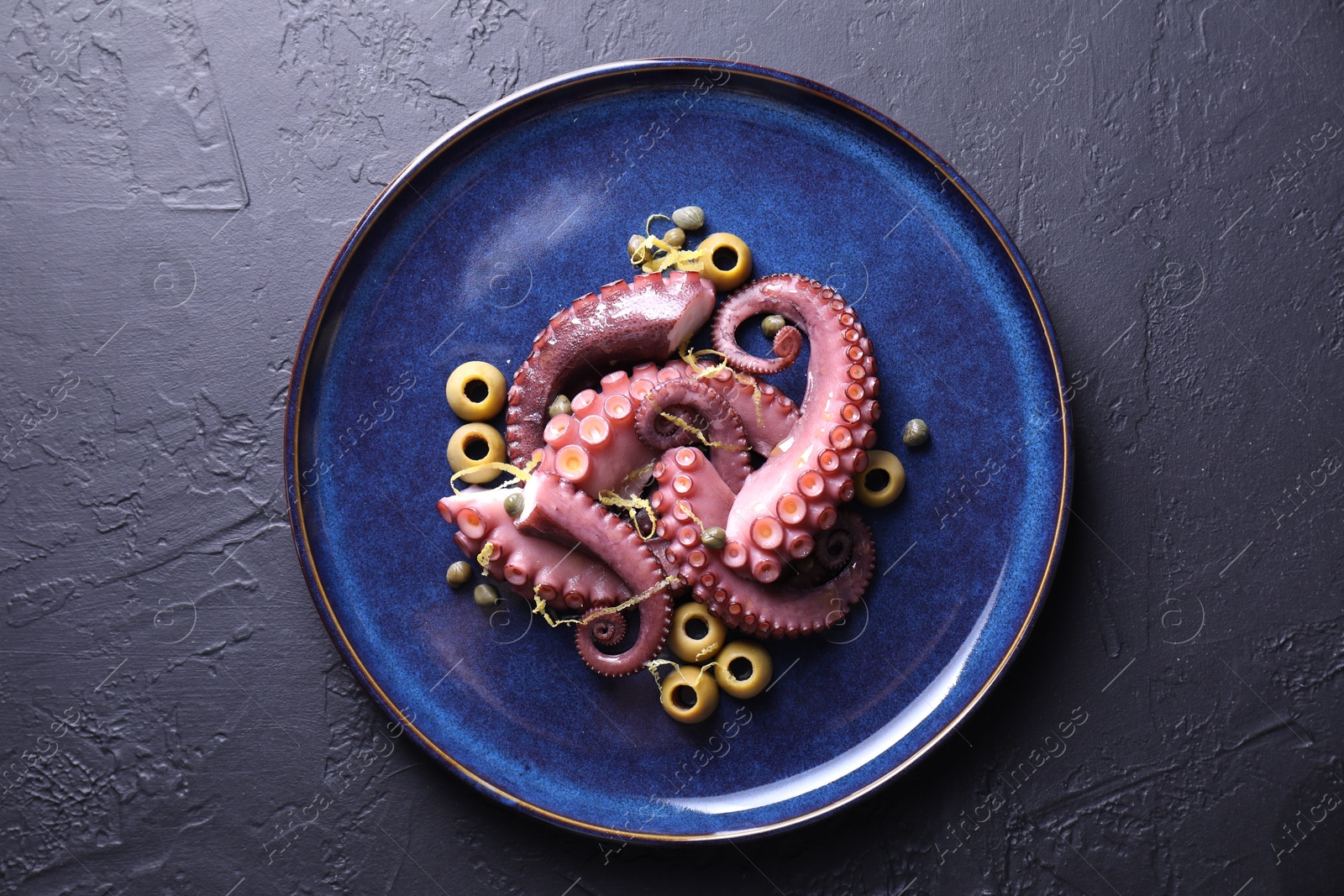 Photo of Appetizing octopus tentacles on dark table, top view