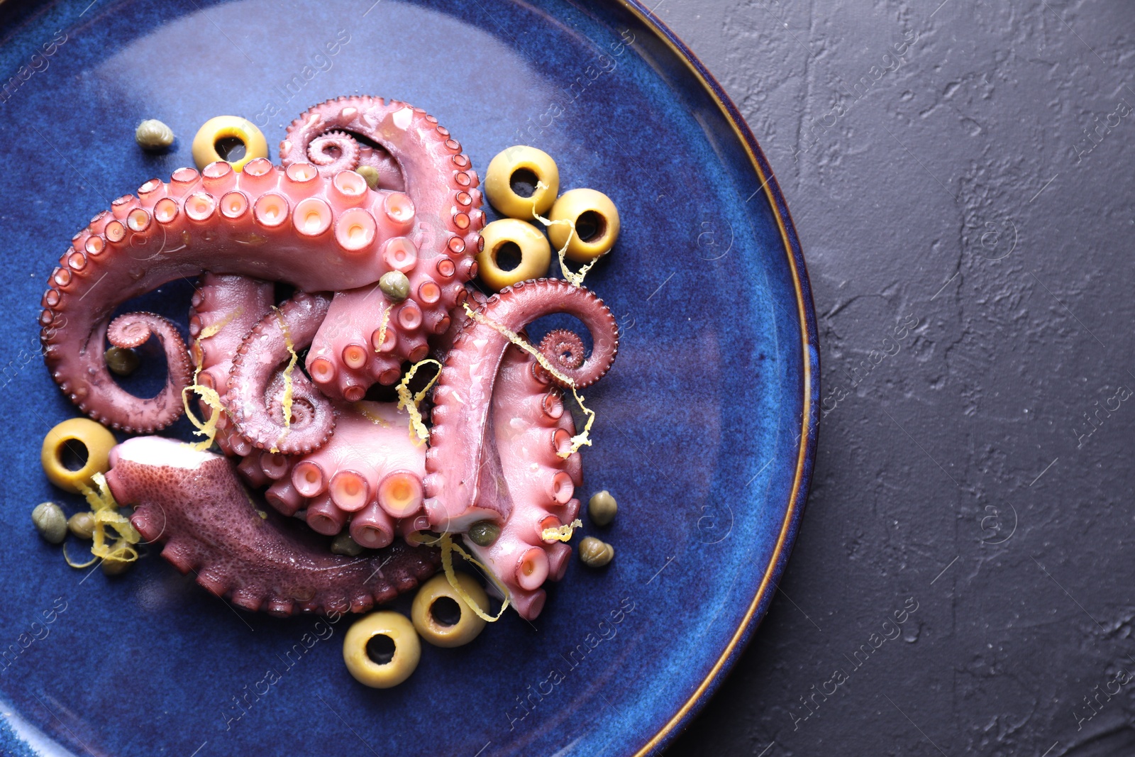 Photo of Appetizing octopus tentacles on dark table, top view