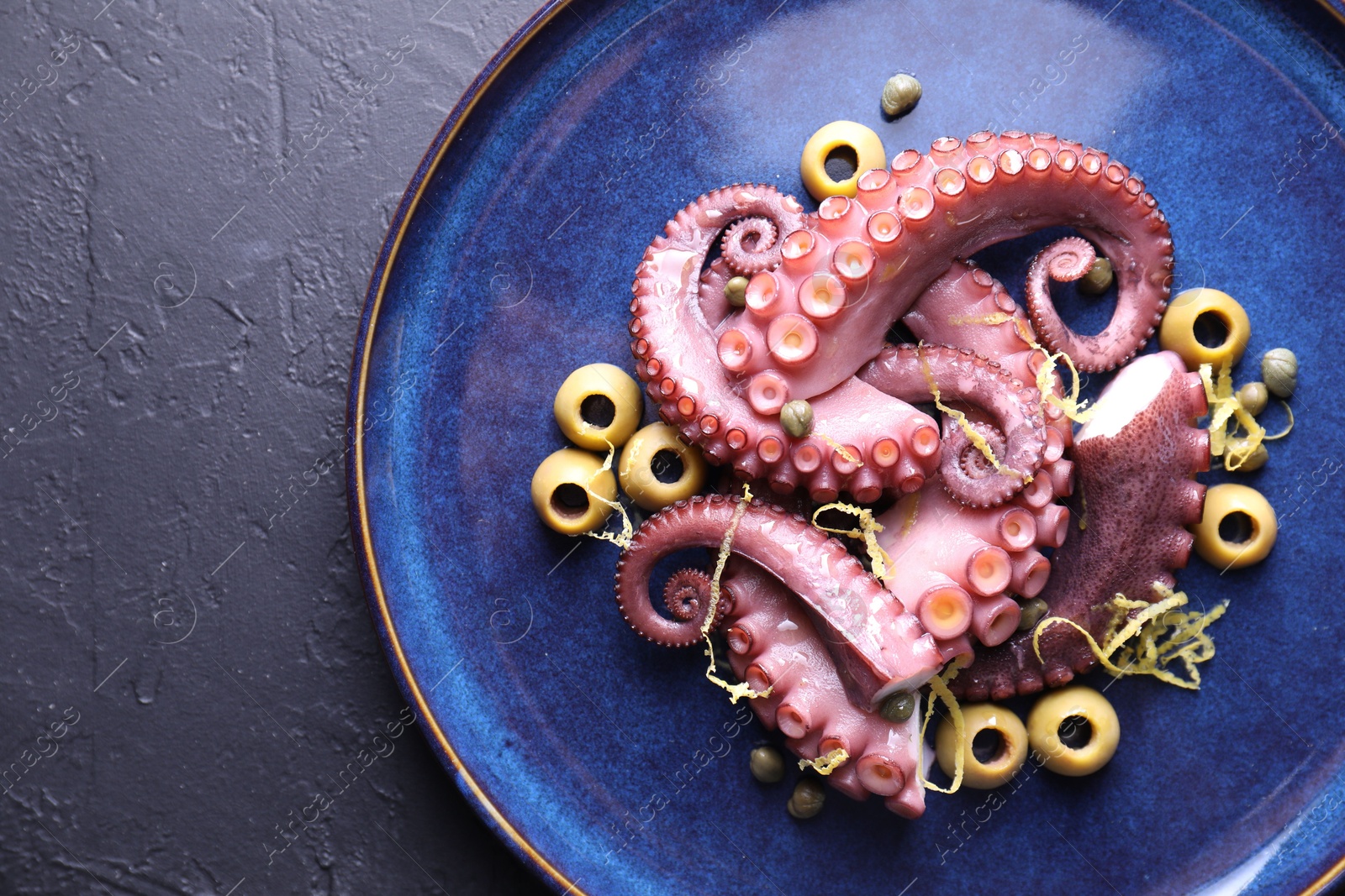 Photo of Appetizing octopus tentacles on dark table, top view