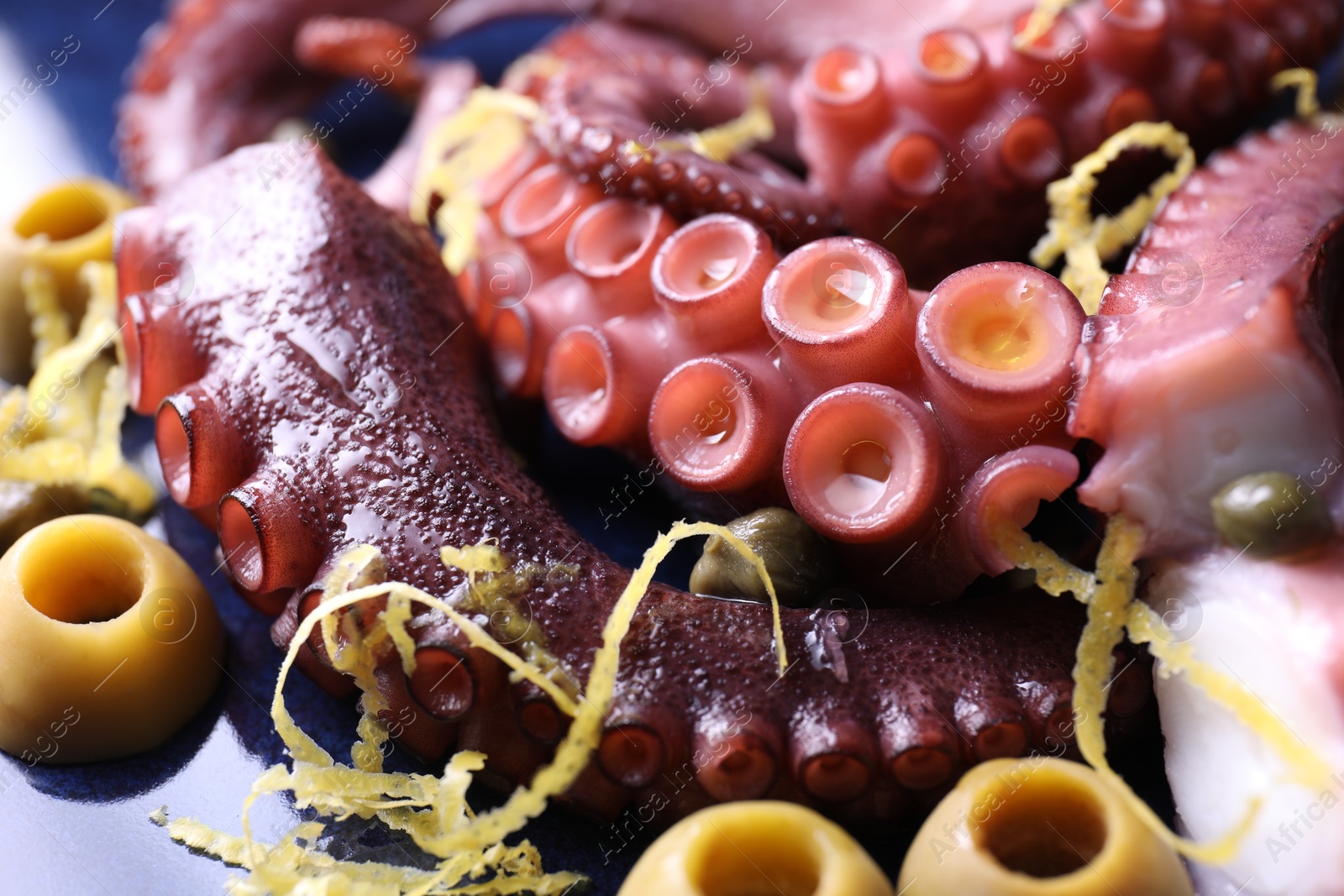 Photo of Appetizing octopus tentacles with lemon zest and olives on plate, closeup