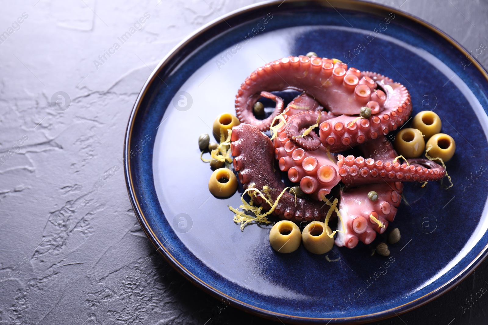 Photo of Appetizing octopus tentacles with olives on dark table, closeup