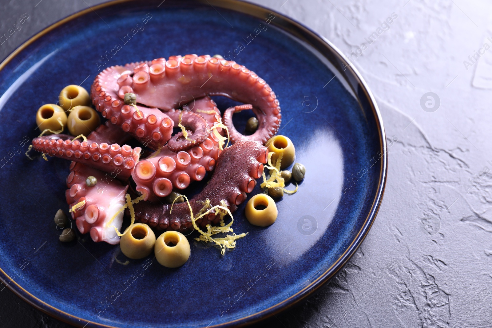 Photo of Appetizing octopus tentacles with olives on dark table, closeup