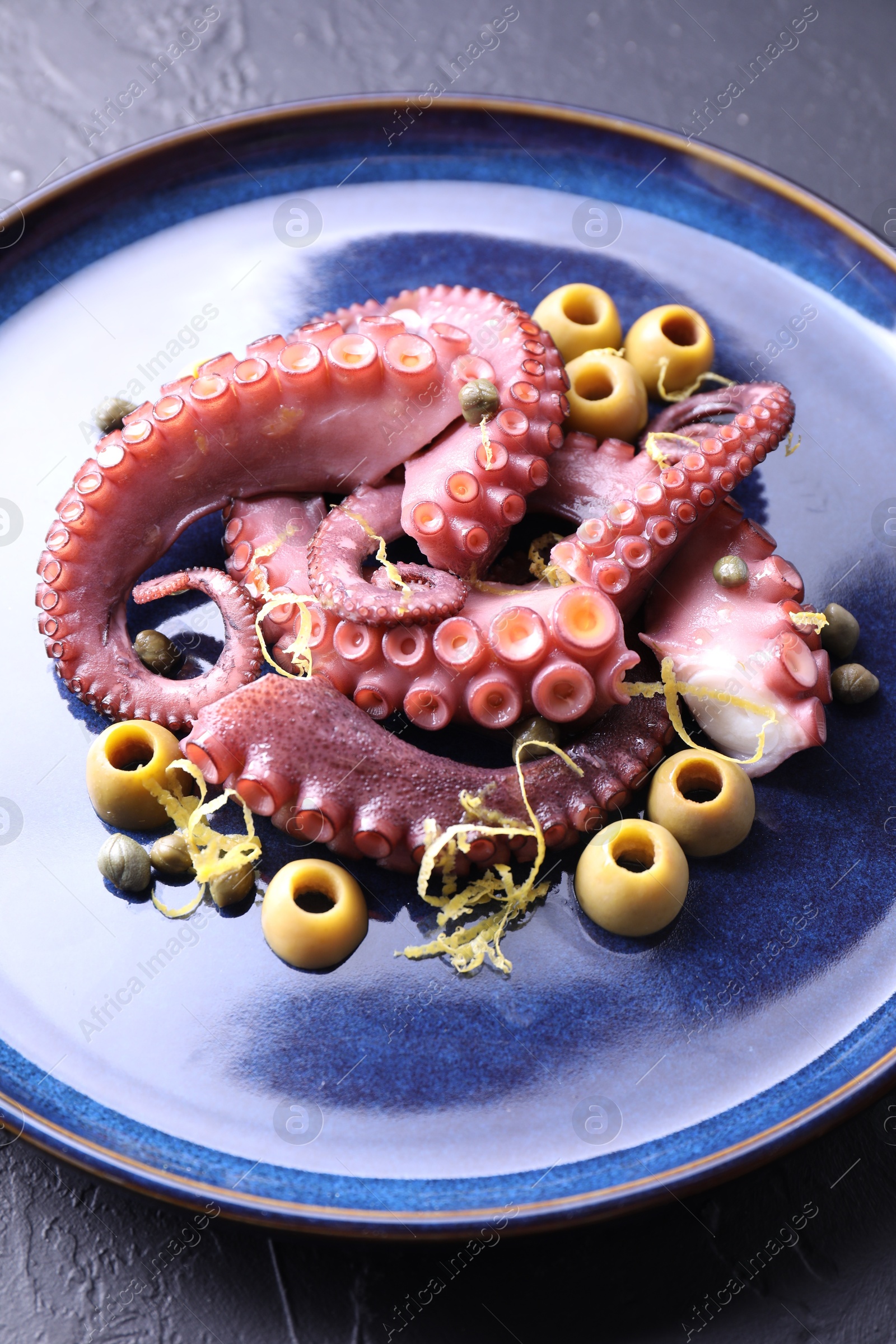 Photo of Appetizing octopus tentacles with olives on dark table, closeup