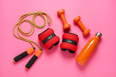 Photo of Red ankle weights and sport equipment on pink background, flat lay