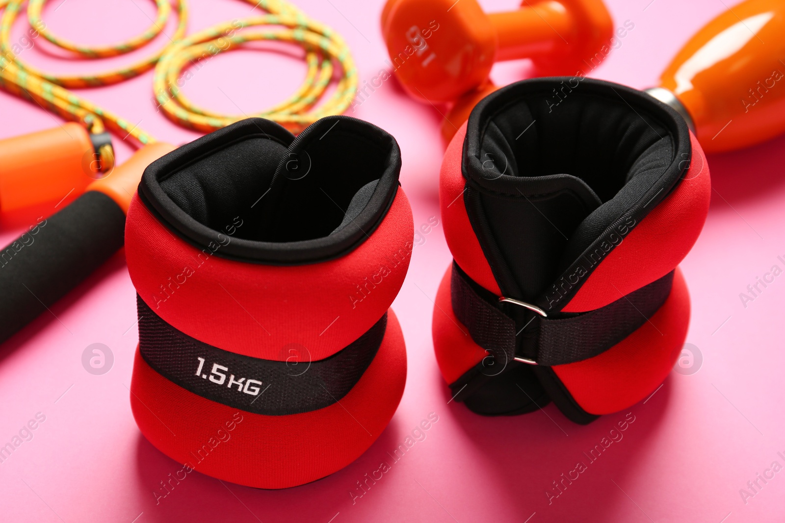 Photo of Red ankle weights and sport equipment on pink background, closeup