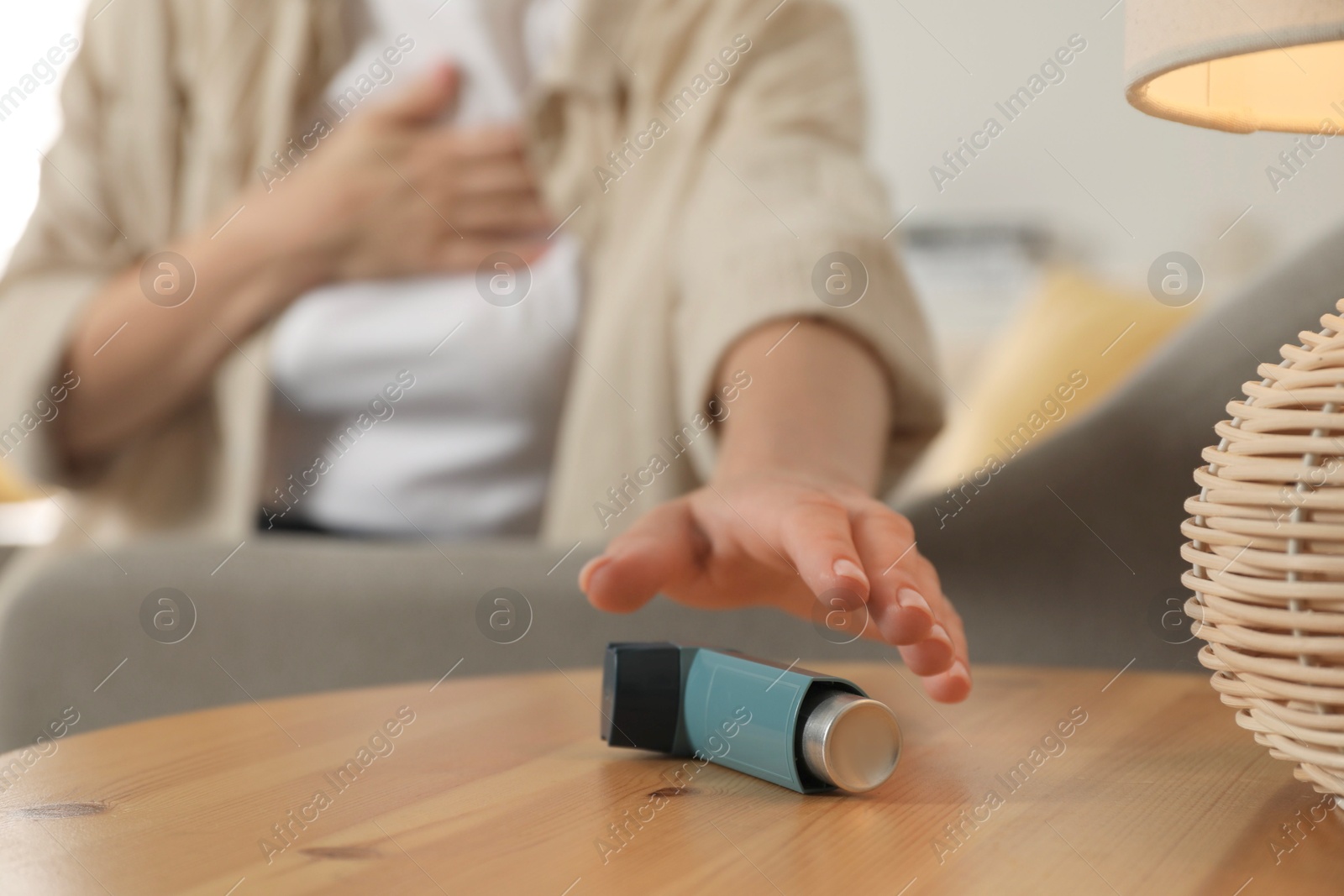 Photo of Woman reaching for asthma inhaler at wooden table indoors, closeup