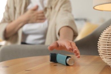 Photo of Woman reaching for asthma inhaler at wooden table indoors, closeup