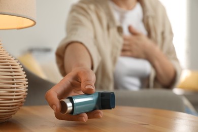 Photo of Woman holding asthma inhaler at wooden table indoors, closeup