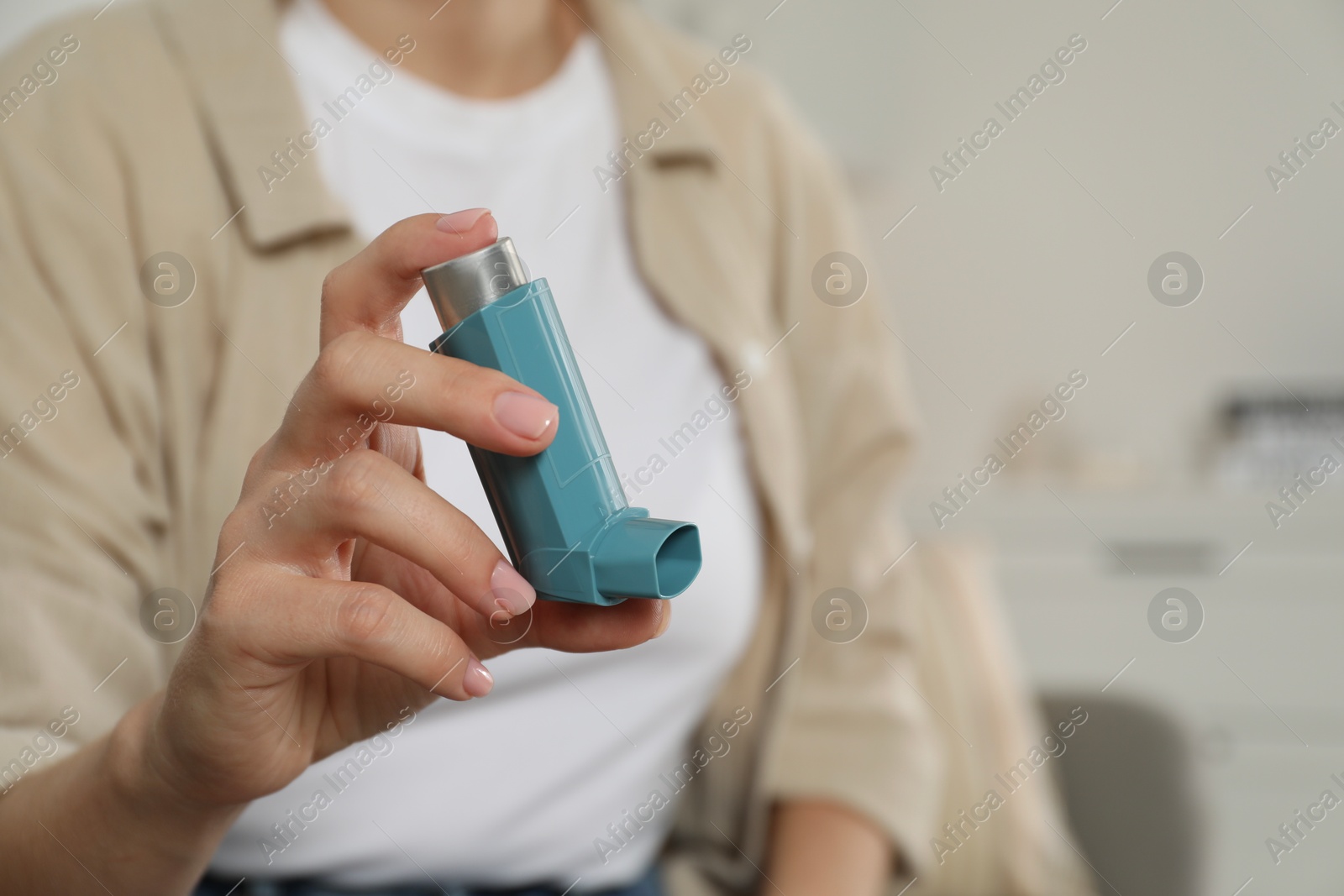 Photo of Woman holding asthma inhaler indoors, closeup. Space for text