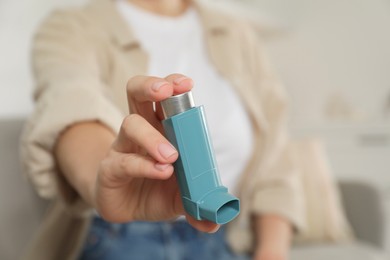 Woman holding asthma inhaler indoors, closeup. Space for text