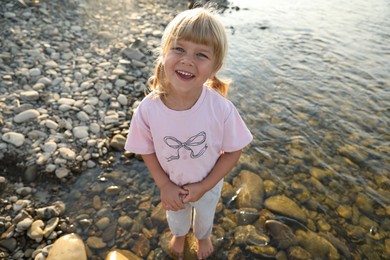 Photo of Cute little girl standing in water, above view. Child enjoying beautiful nature