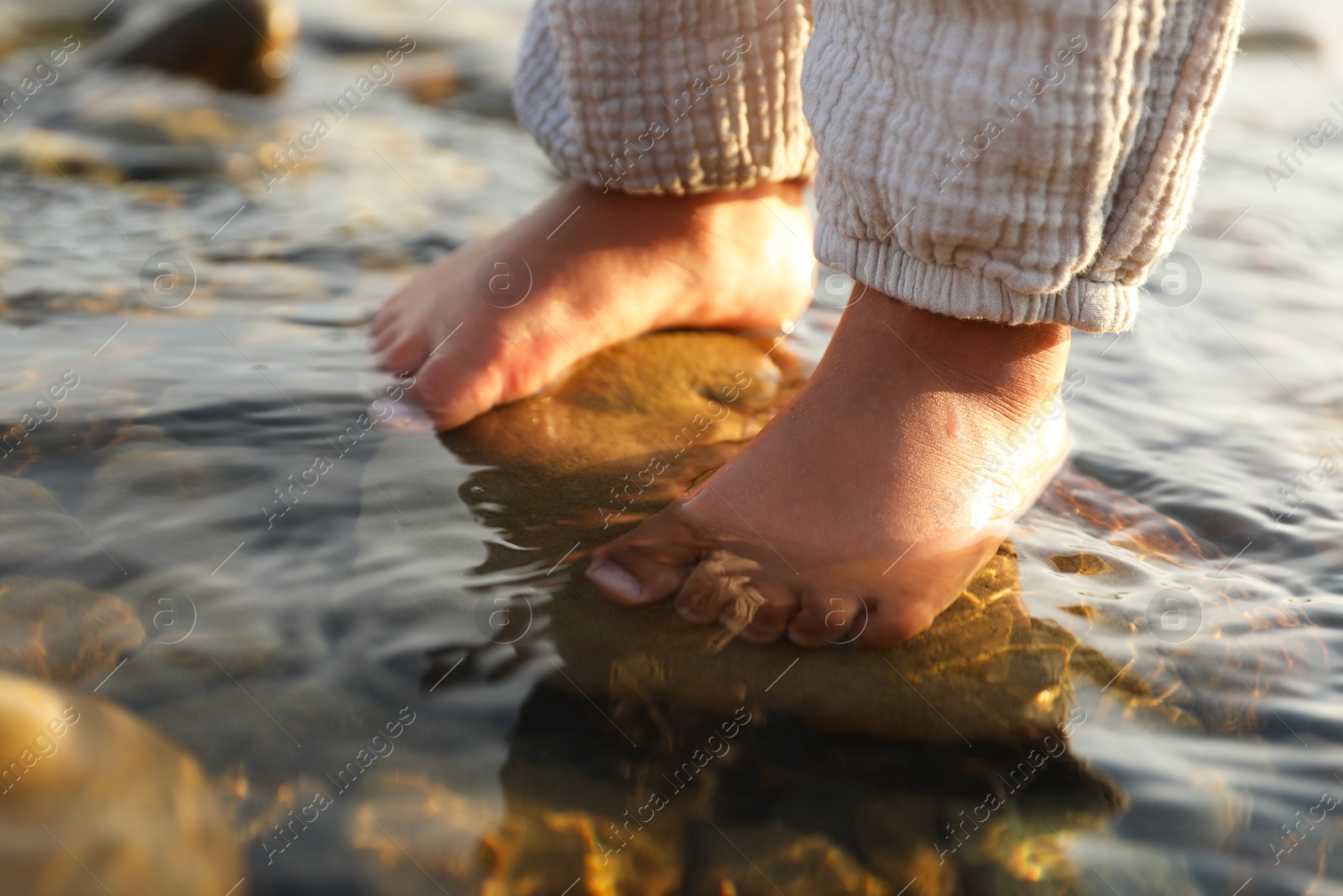 Photo of Cute little girl standing in water outdoors, closeup. Child enjoying beautiful nature