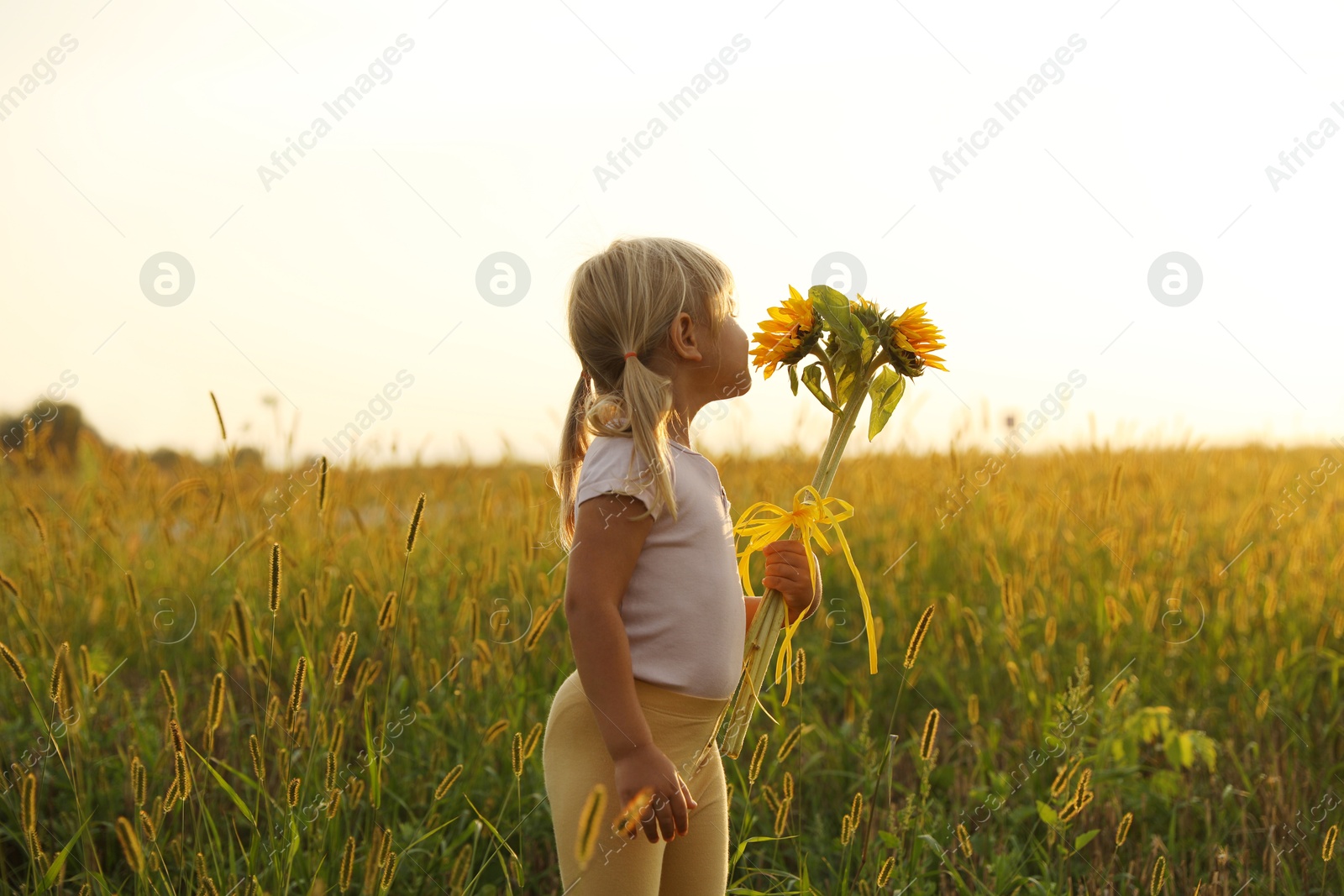 Photo of Cute little girl with sunflowers at meadow. Child enjoying beautiful nature