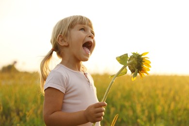 Photo of Cute little girl with sunflower at meadow. Child enjoying beautiful nature