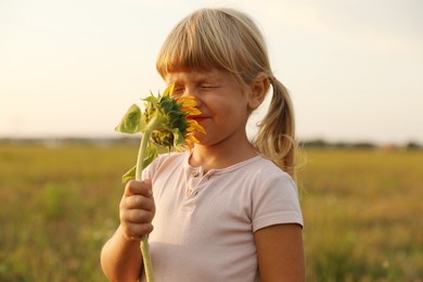 Photo of Cute little girl with sunflower at meadow. Child enjoying beautiful nature