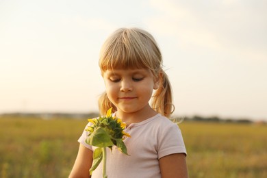 Photo of Cute little girl with sunflower at meadow. Child enjoying beautiful nature