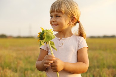 Photo of Cute little girl with sunflower at meadow. Child enjoying beautiful nature