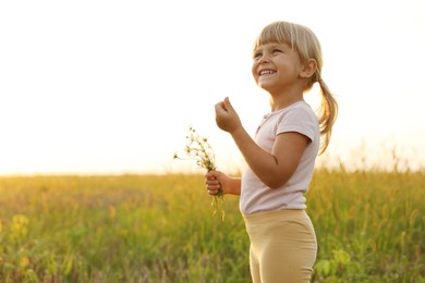 Photo of Cute little girl with chamomiles at meadow, space for text. Child enjoying beautiful nature