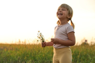 Photo of Cute little girl with chamomiles at meadow, space for text. Child enjoying beautiful nature