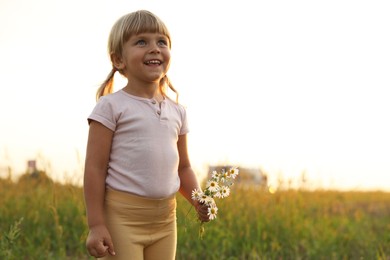 Cute little girl with chamomiles at meadow, space for text. Child enjoying beautiful nature