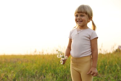 Photo of Cute little girl with chamomiles at meadow, space for text. Child enjoying beautiful nature