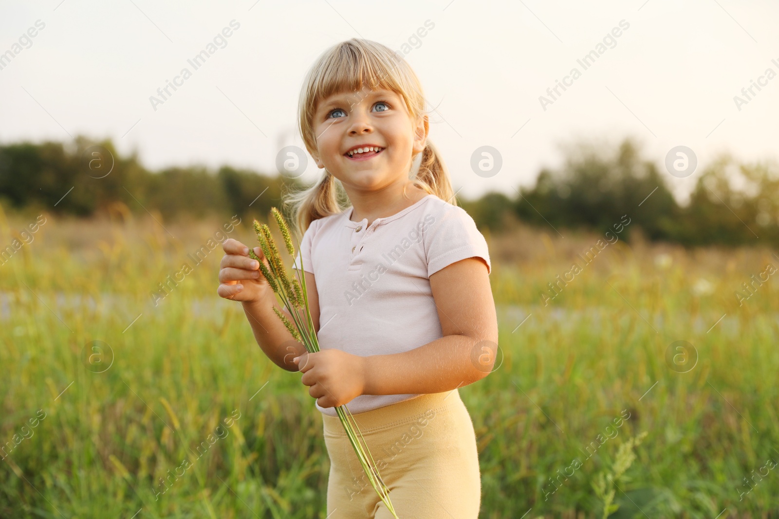 Photo of Cute little girl with plants at meadow. Child enjoying beautiful nature