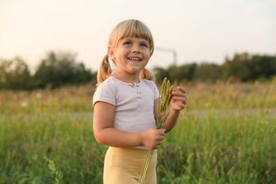 Photo of Cute little girl with plants at meadow. Child enjoying beautiful nature