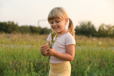 Photo of Cute little girl with plants at meadow. Child enjoying beautiful nature