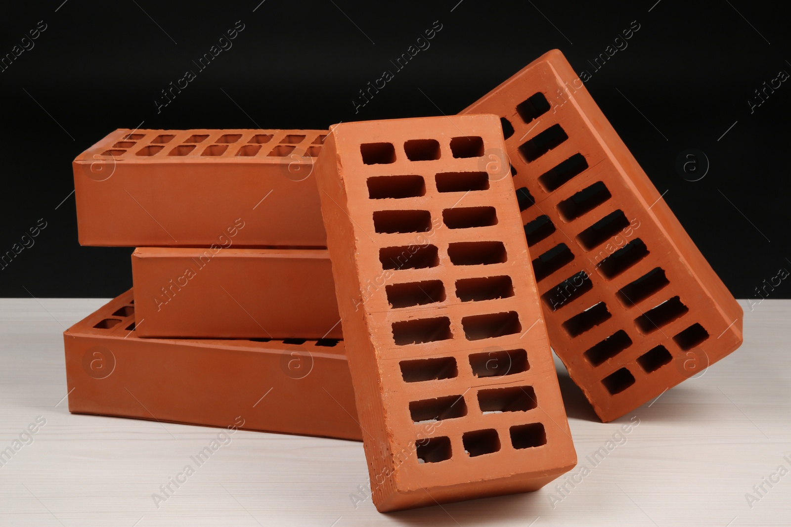 Photo of Many red bricks on light wooden table against black background. Building material