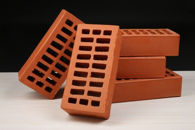 Photo of Many red bricks on light wooden table against black background. Building material