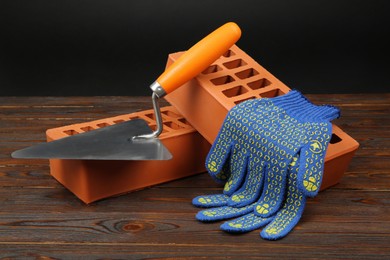 Photo of Red bricks, putty knife and rubber gloves on wooden table. Building material