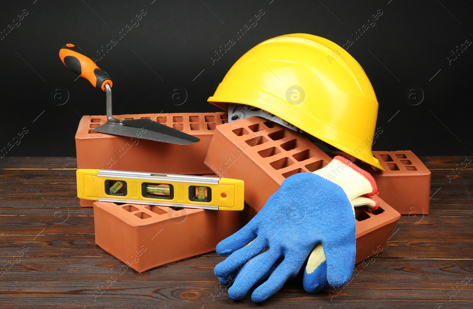 Photo of Red bricks, different construction tools and safety equipment on wooden table