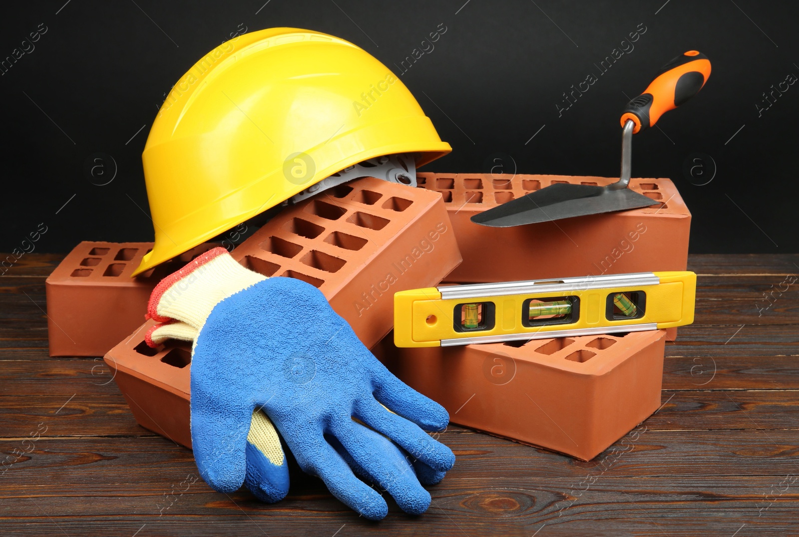 Photo of Red bricks, different construction tools and safety equipment on wooden table