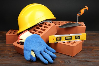 Photo of Red bricks, different construction tools and safety equipment on wooden table