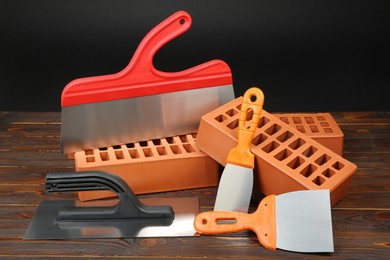 Photo of Red bricks and putty knives on wooden table. Building material and construction tools